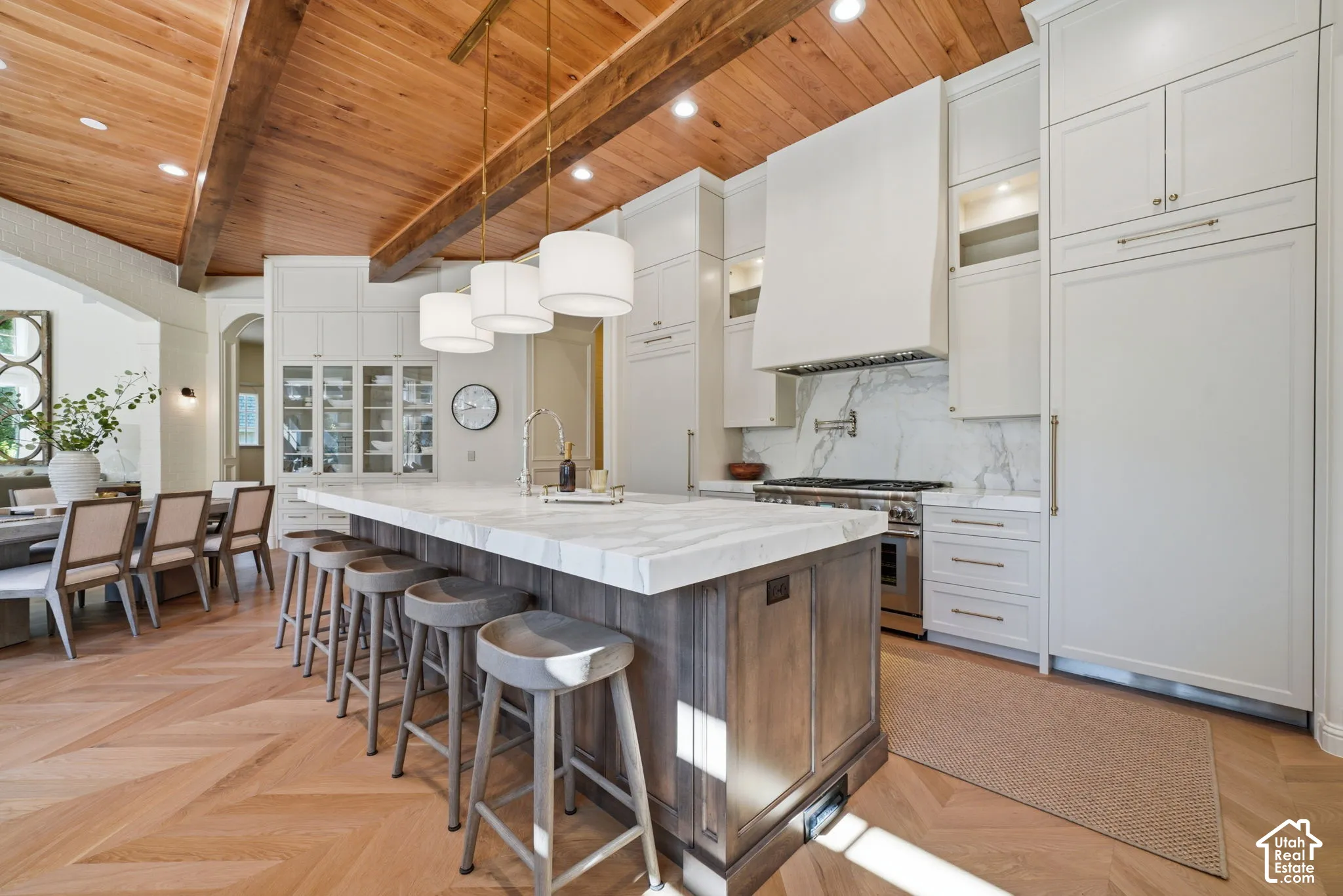 Kitchen featuring vaulted wood-plank ceilings with exposed beams, herringbone wood-finish flooring, a large island with stone countertops, floor-to-ceiling custom cabinetry, and a full-height stone backsplash