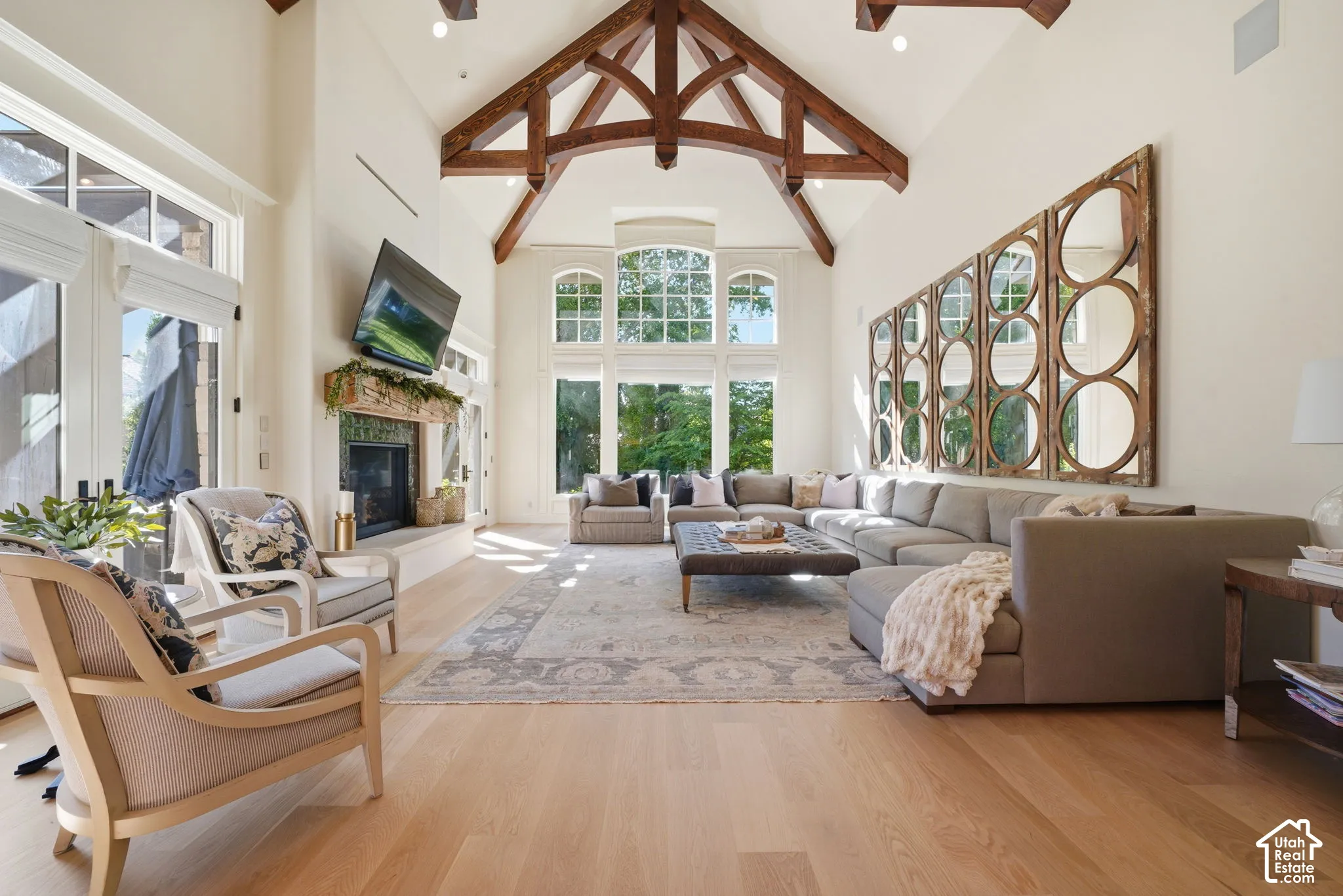 Vaulted ceiling featuring exposed timber trusses, wood-finish flooring, floor-to-ceiling windows, and a fireplace with a stone-surround mantel