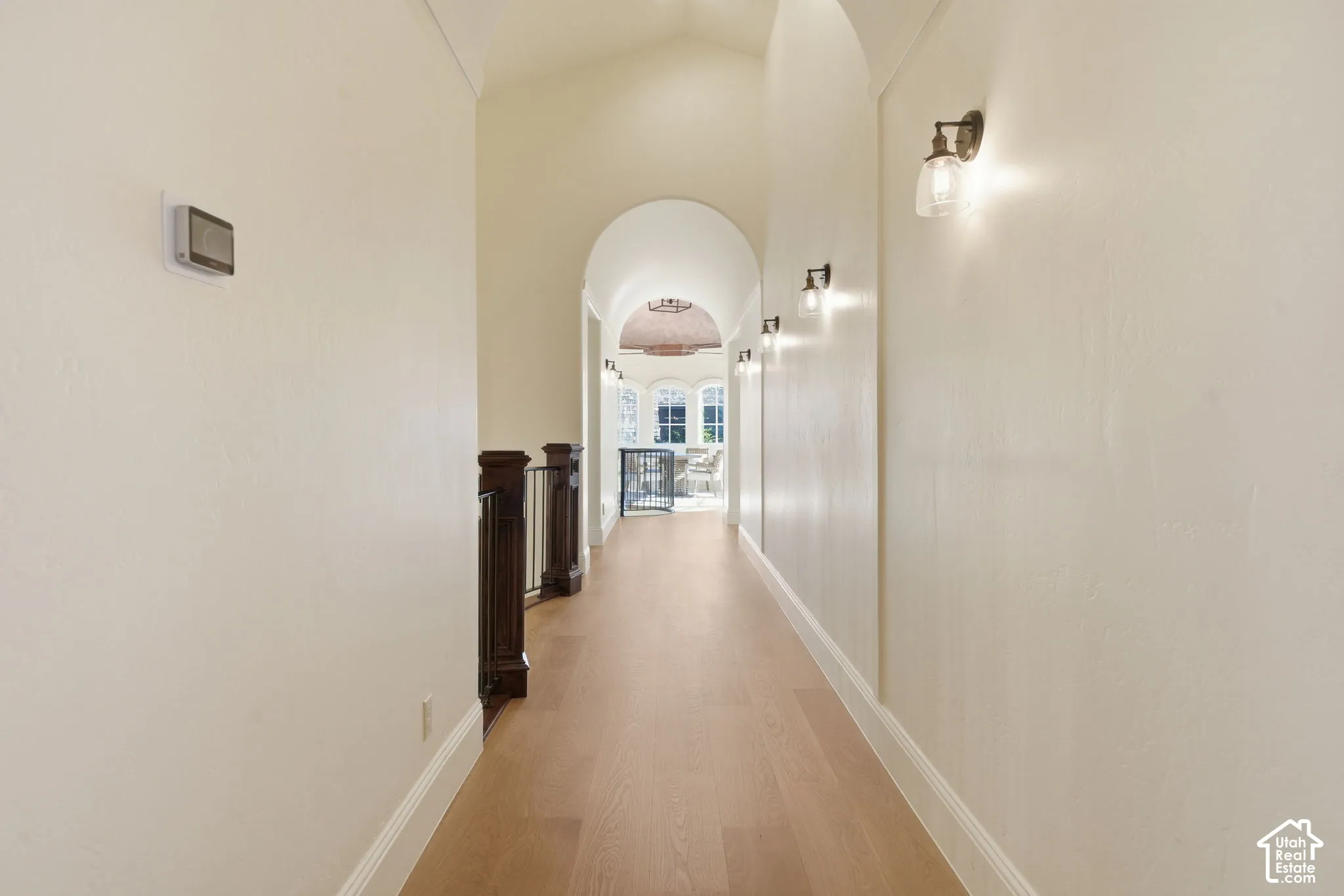 Hallway featuring wood-finish flooring, vaulted ceilings, arched architectural details, and wall-mounted light fixtures with glass shades