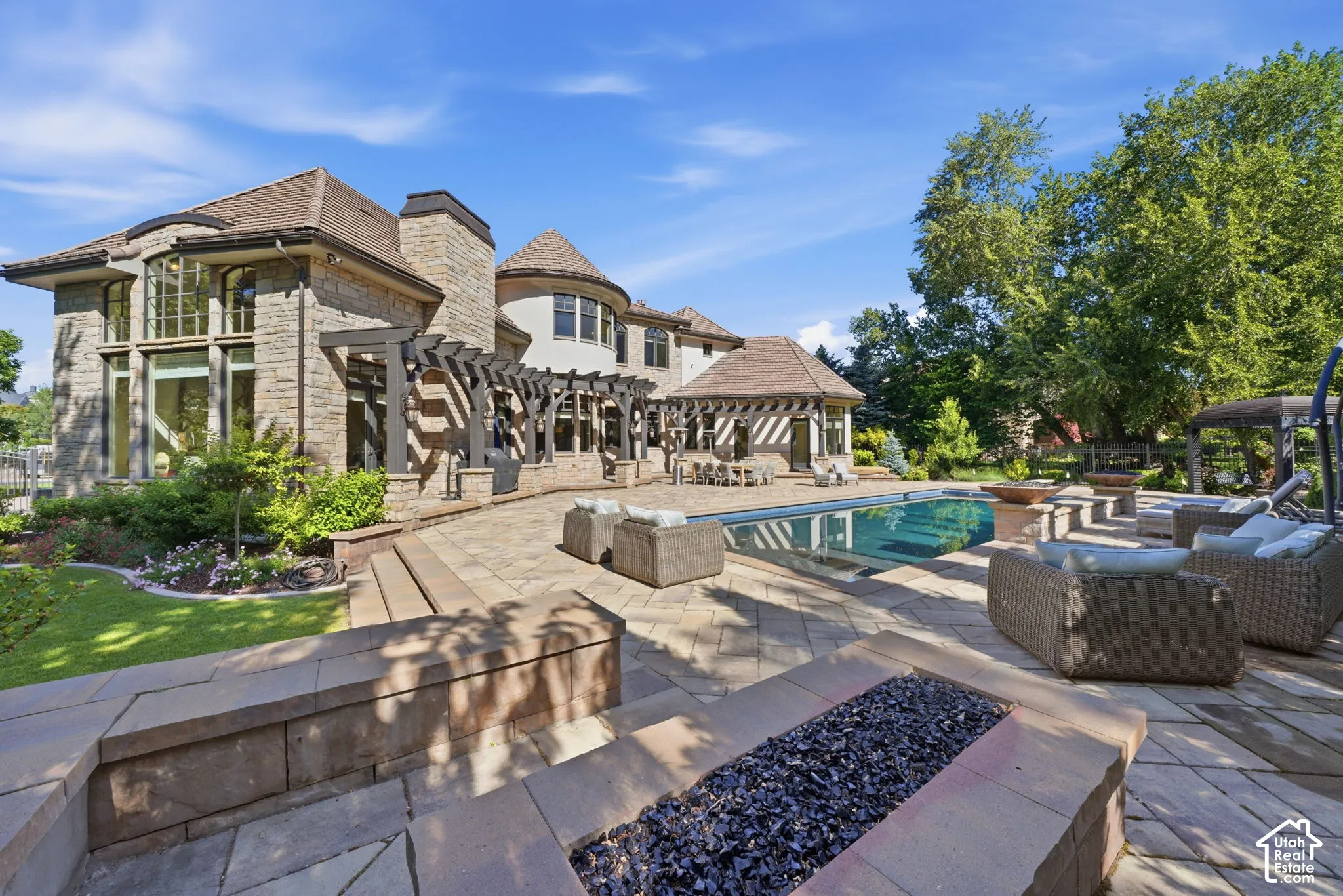 Stone exterior facade with multi-level rooflines, integrated pergolas, in-ground swimming pool, and stone-finished fire pit
