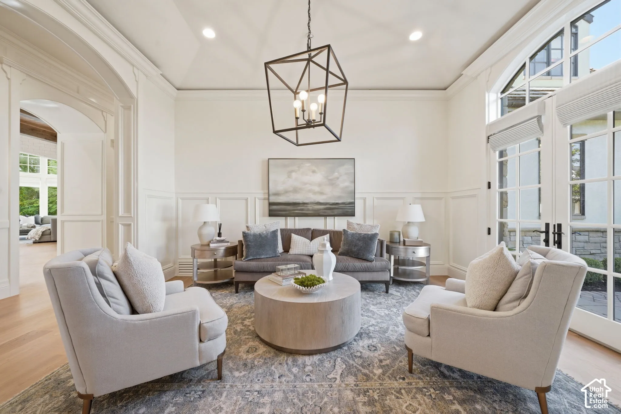 Tray ceiling, geometric iron chandelier, wainscoting, arched entryway, and glass-paneled double doors