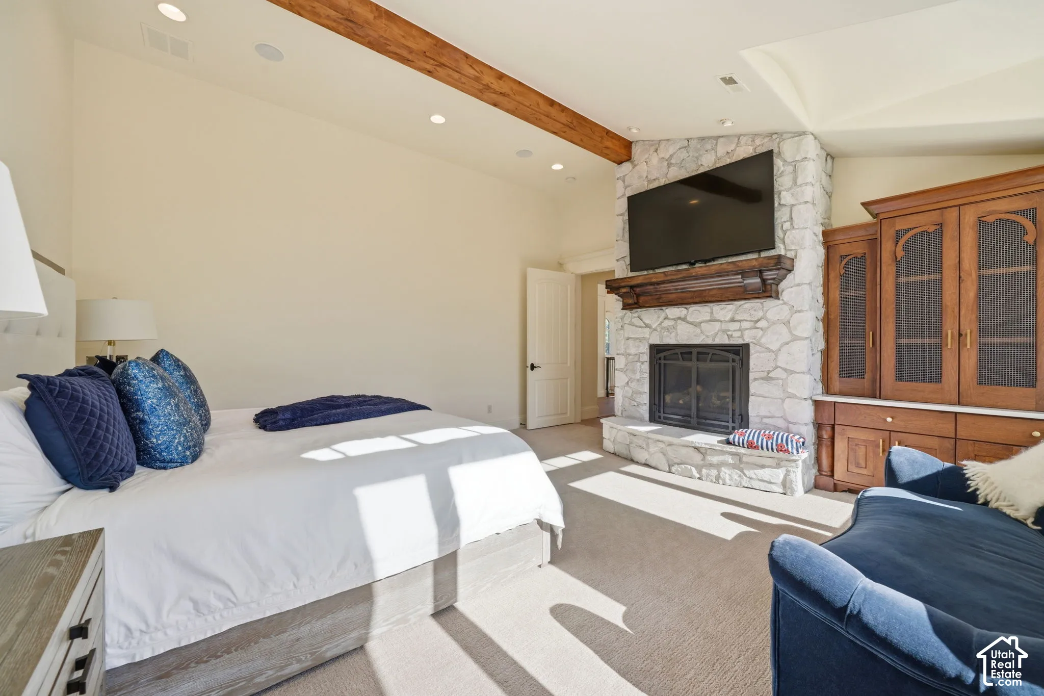 Vaulted ceiling featuring an exposed wood beam, stone fireplace with a thick wood mantel, and built-in cabinetry
