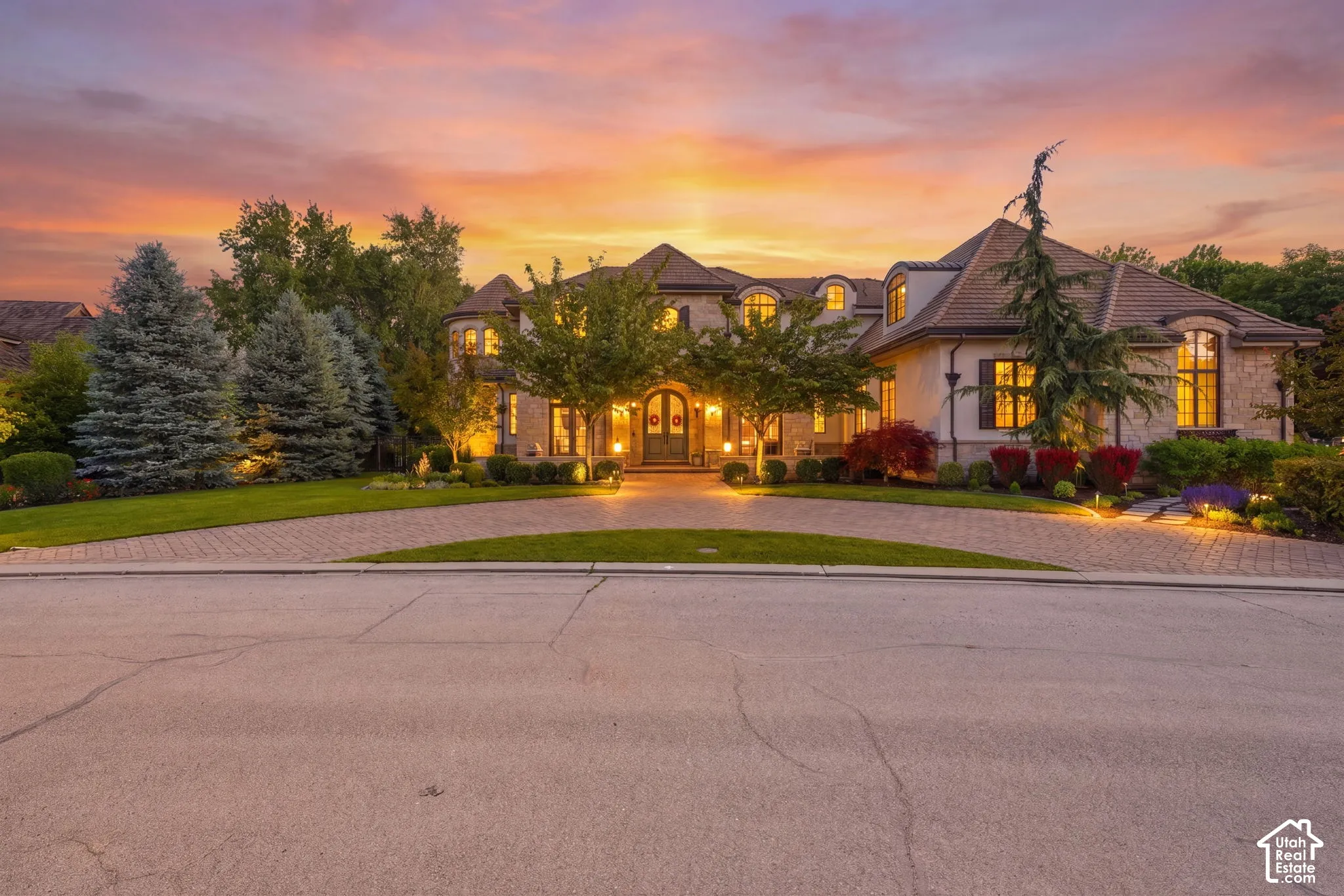 Custom masonry exterior with a multi-gabled tile roof, featuring an expansive stone-paved circular driveway and manicured professional landscaping