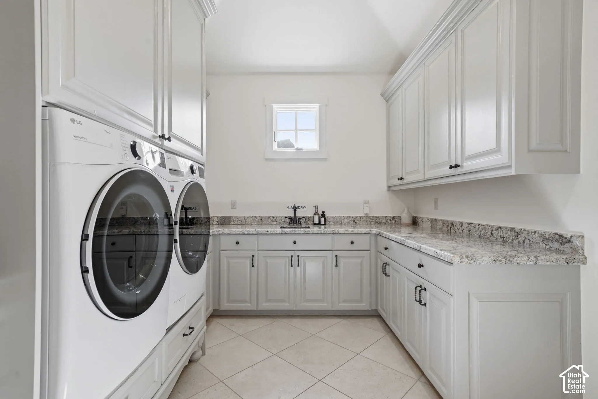 Laundry area featuring extensive grey cabinetry, stone-finish countertops, an integrated sink with a high-arch faucet, and tile flooring