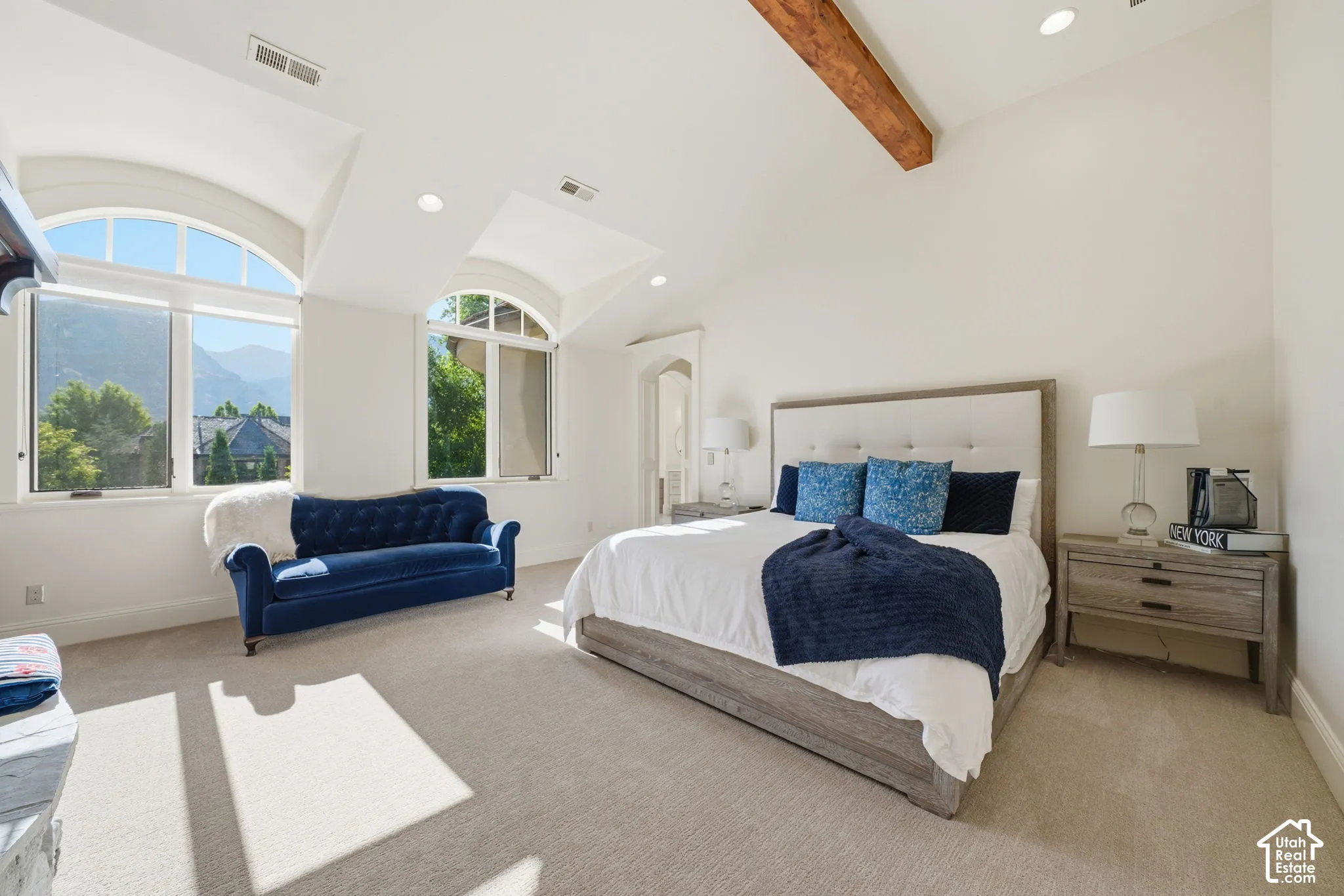 Vaulted ceiling with a rustic wood-beam accent, two arched windows with mountain scenery, and recessed lighting