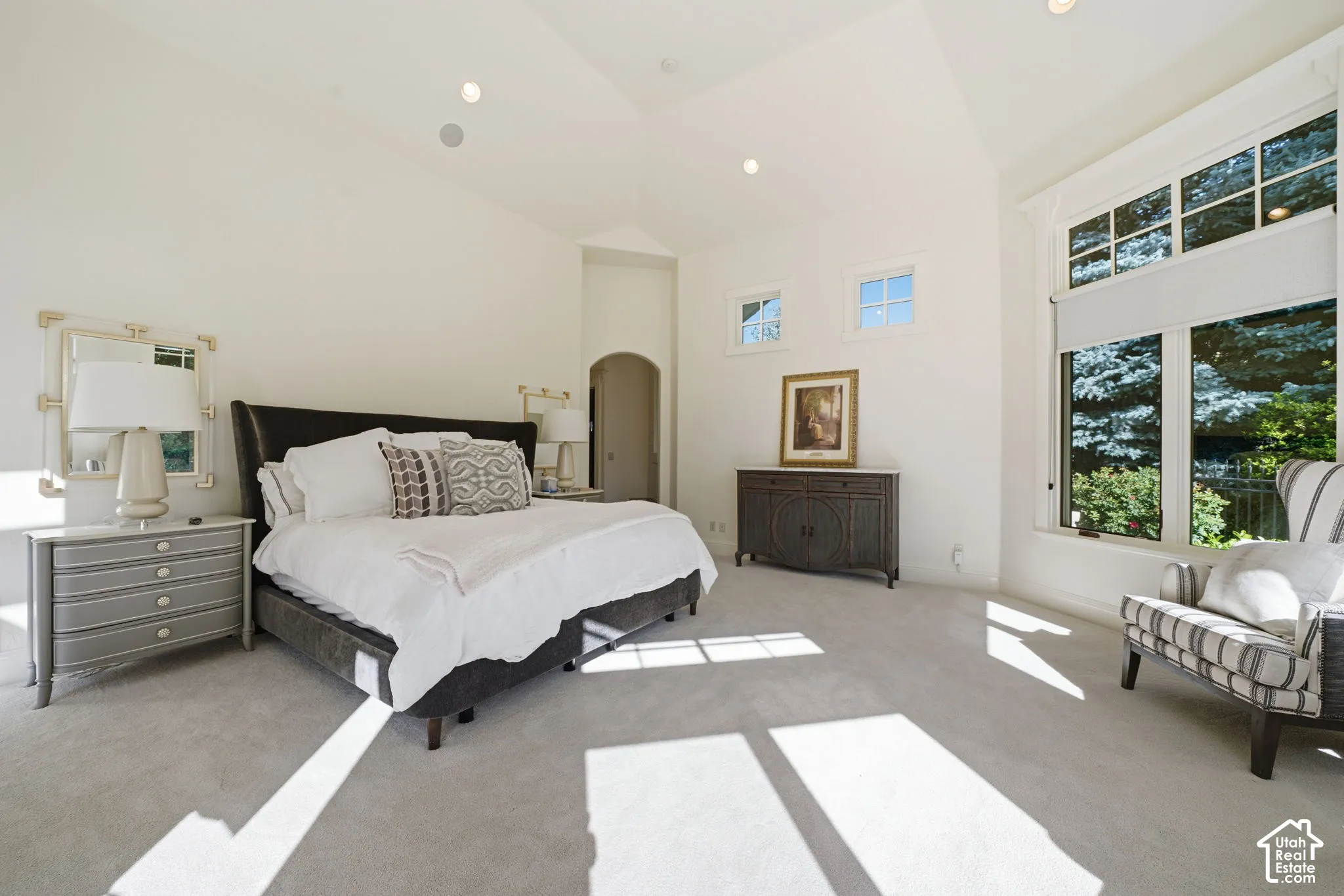 Vaulted ceilings with recessed lighting, oversized windows with grid detailing, carpeted flooring, and an arched doorway