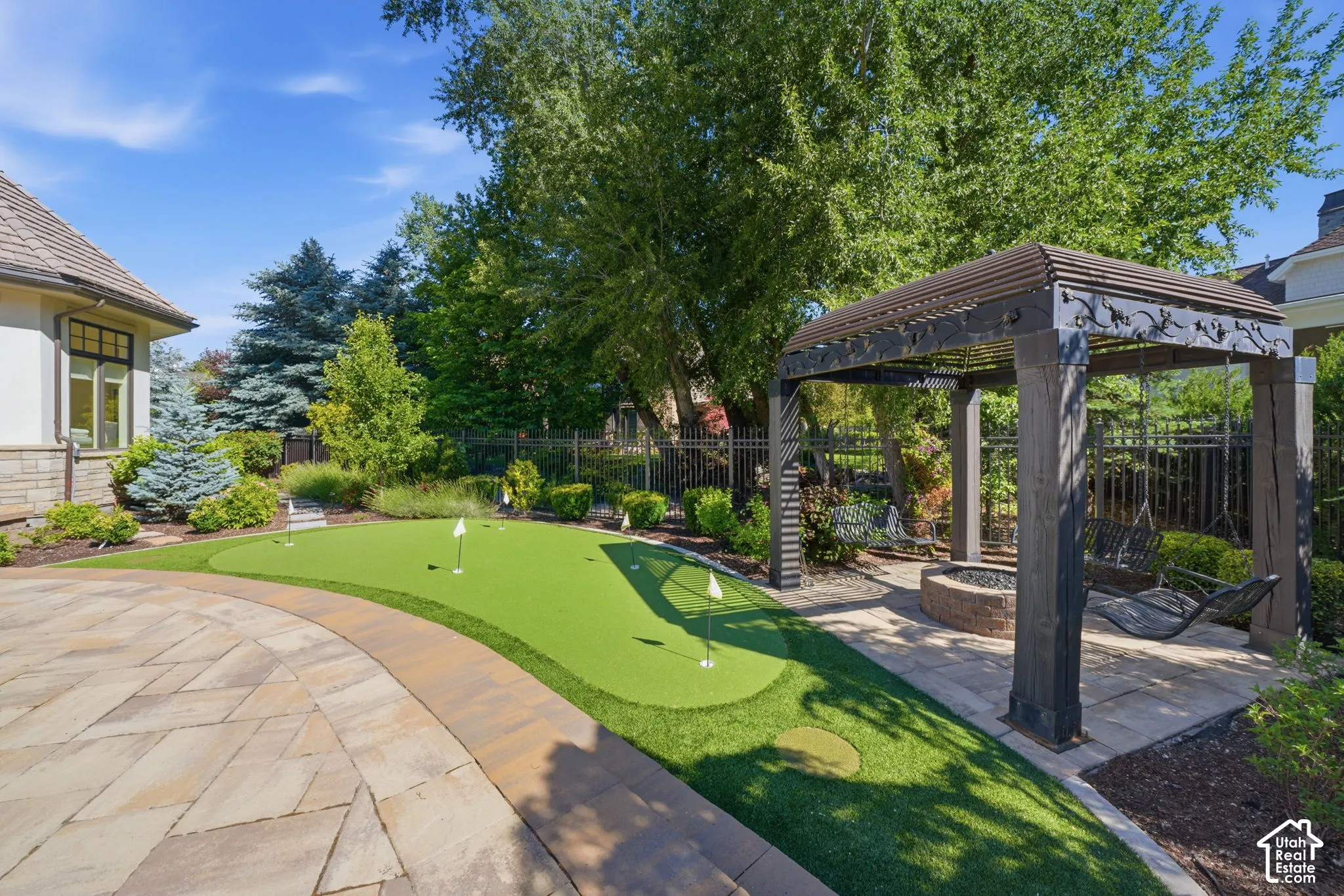 Backyard featuring a synthetic putting green, stone paver patio, custom timber pergola, and built-in stone fire pit