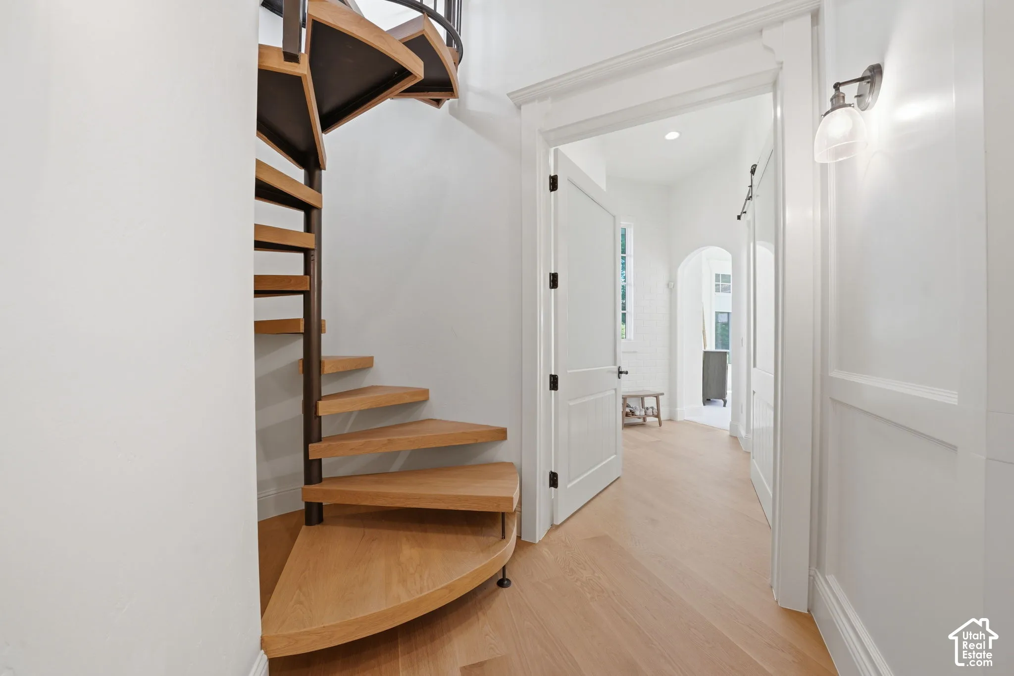 Spiral staircase with wood treads and metal support, wood-finish flooring, paneled wainscoting, solid-core interior doors, and wall-mounted sconce lighting