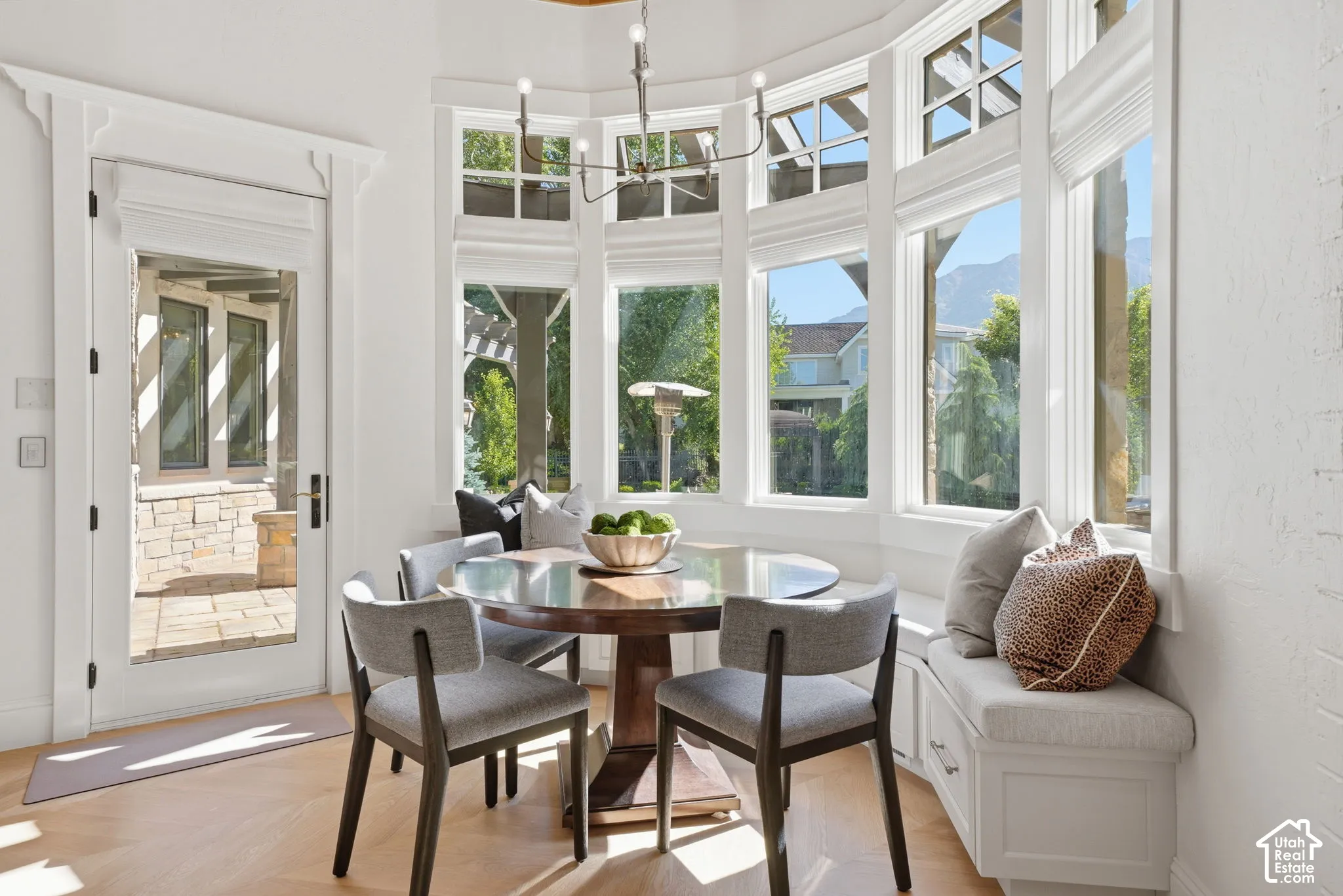 Sunlit breakfast nook featuring a bay window, built-in bench seating with storage drawers, herringbone wood-finish flooring, a multi-arm chandelier, and a glass-paneled exterior door
