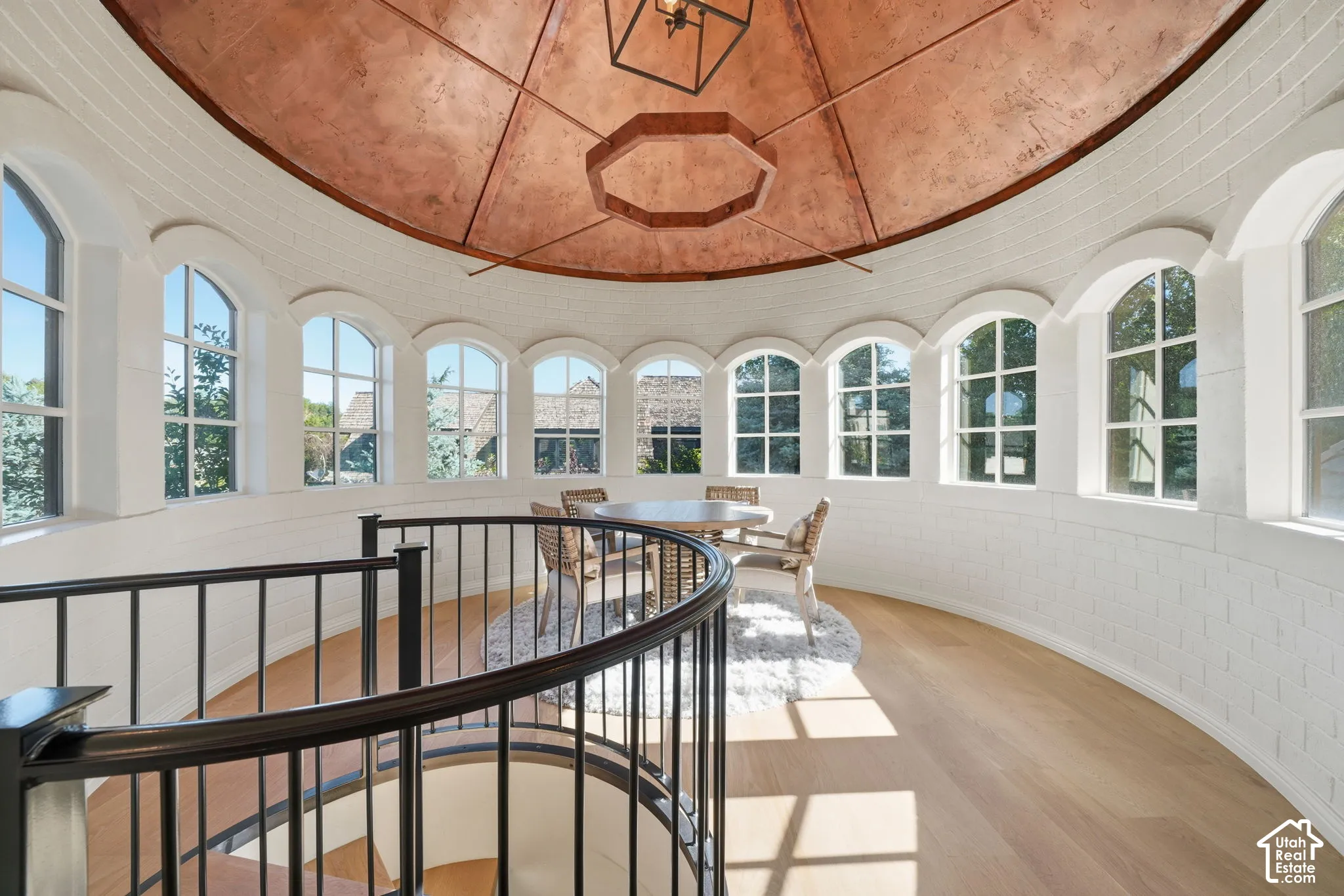 Circular rotunda featuring a metallic dome ceiling, arched windows, light-toned wood-finish flooring, and a curved metal staircase railing