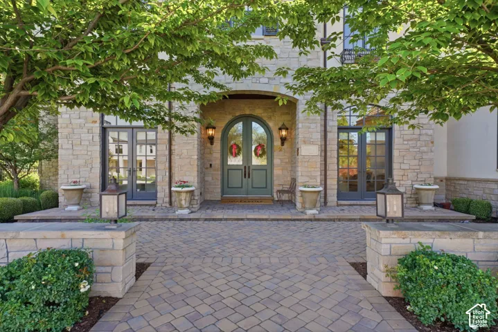 Stone masonry exterior featuring an arched entryway, double-door entrance, paver stone walkway, and structured landscaping
