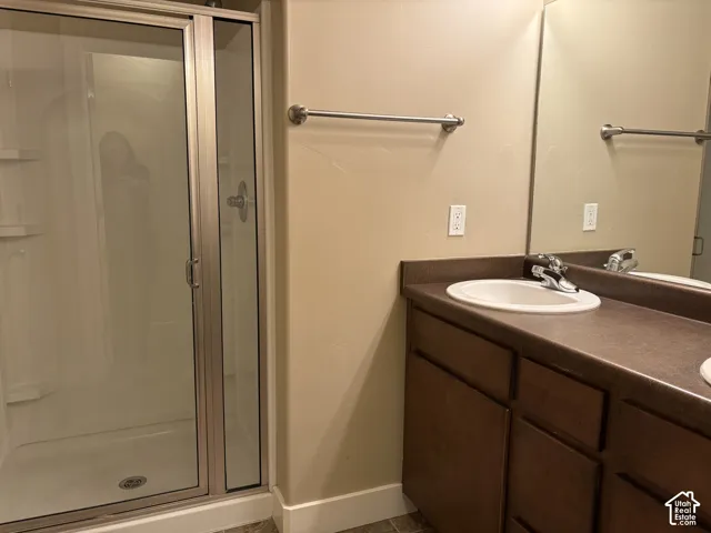 Bathroom featuring a shower stall with a framed glass door, wood-finish cabinetry, an oval drop-in sink, and a wall-mounted mirror