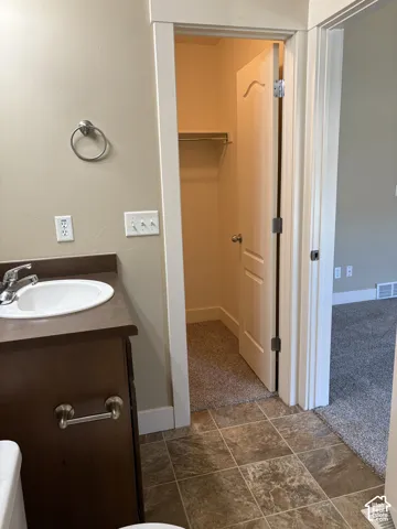 Vanity featuring a dark-toned cabinet with a neutral countertop and inset sink, paired with tile flooring and a built-in closet with carpeted interior