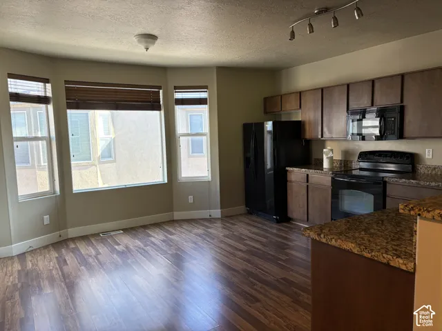 Kitchen featuring wood-finish cabinetry, stone-finish countertops, black built-in appliances, track lighting, and a bay window configuration