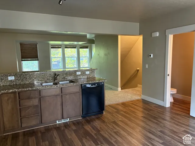 Kitchen featuring a multi-tone stone countertop, wood-finish cabinetry, built-in dishwasher, and wood-finish flooring