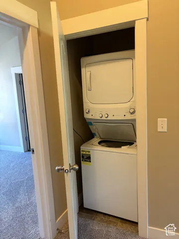 Stacked laundry center featuring a white top-load washer and dryer unit, neutral-toned wall paint, and door-enclosed closet cabinetry