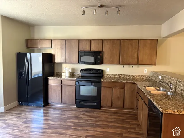 Kitchen featuring stained wood cabinetry, stone-surface countertops, wood-finish flooring, a double-basin stainless steel sink, and integrated black appliances