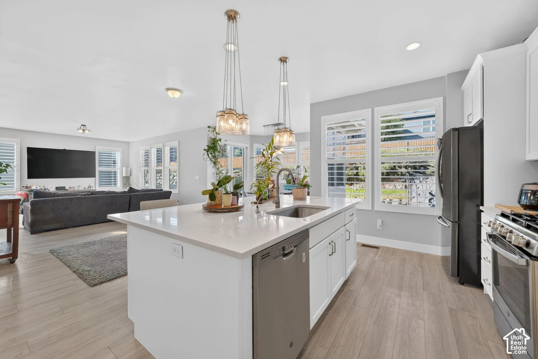 Kitchen featuring a central island with a quartz countertop, undermount stainless steel sink, wood-finish flooring, white shaker cabinetry, and adjustable plantation shutters