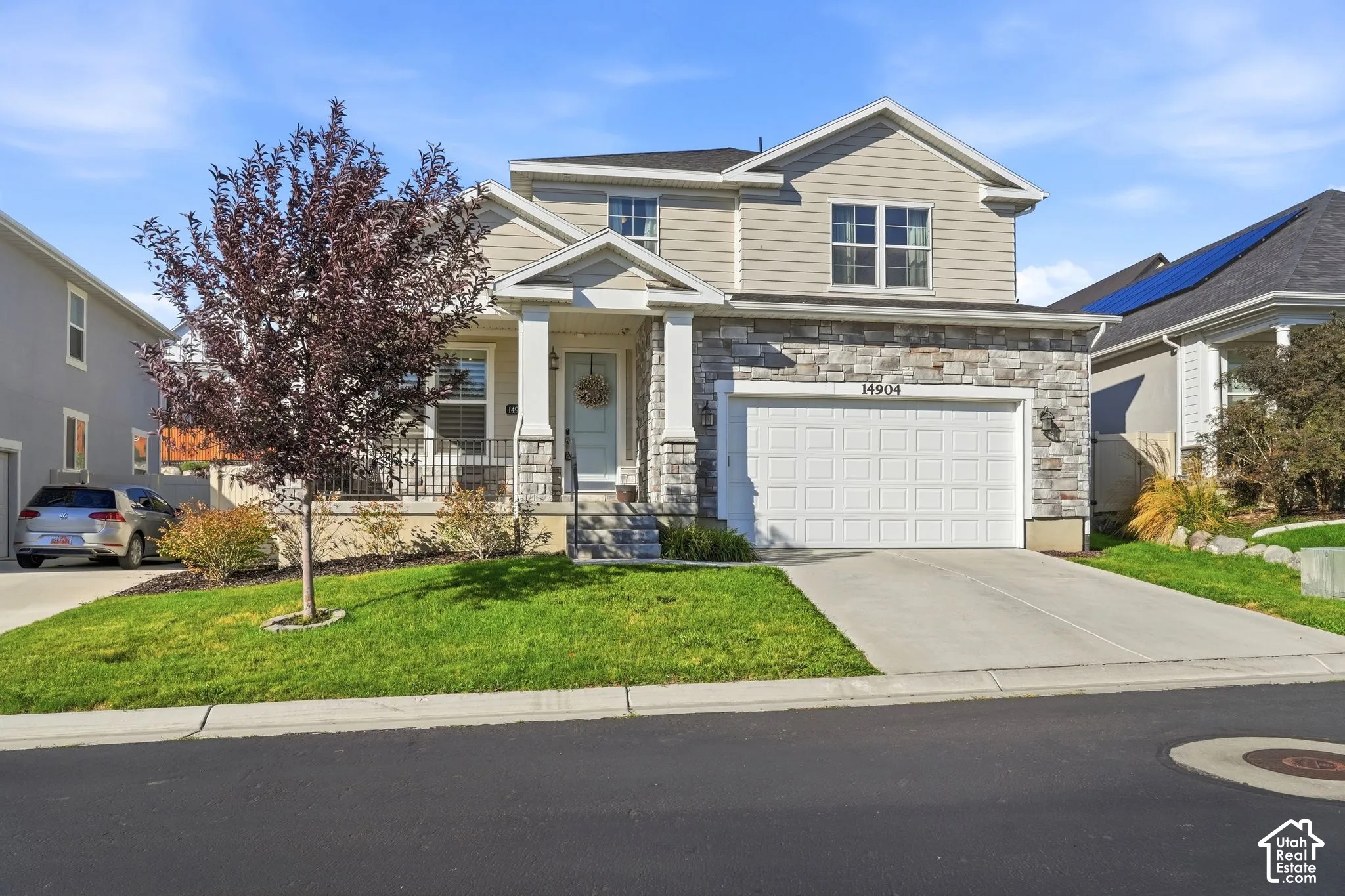 Two-story exterior featuring stone veneer siding, horizontal lap siding, a front porch with square columns, and a multi-car garage