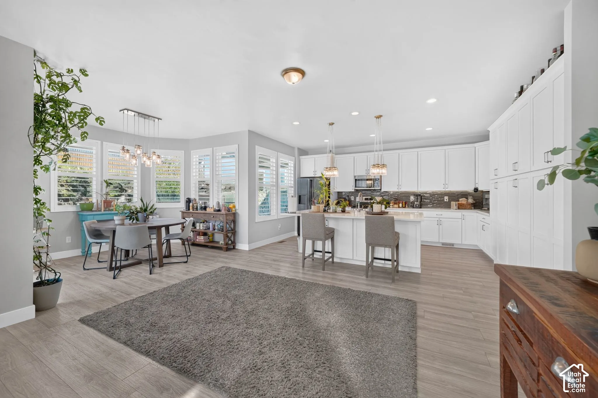 Kitchen featuring a central island with countertop seating, white shaker-style cabinetry, wood-finish flooring, recessed lighting, and bay windows with plantation shutters