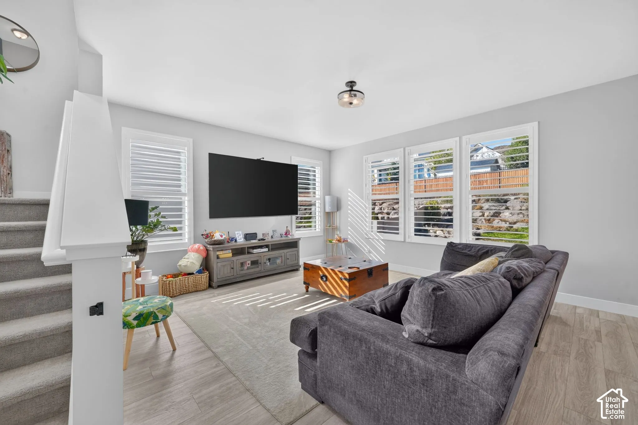 Living area featuring light-toned wood-finish flooring, plantation shutters, and a staircase with a white railing