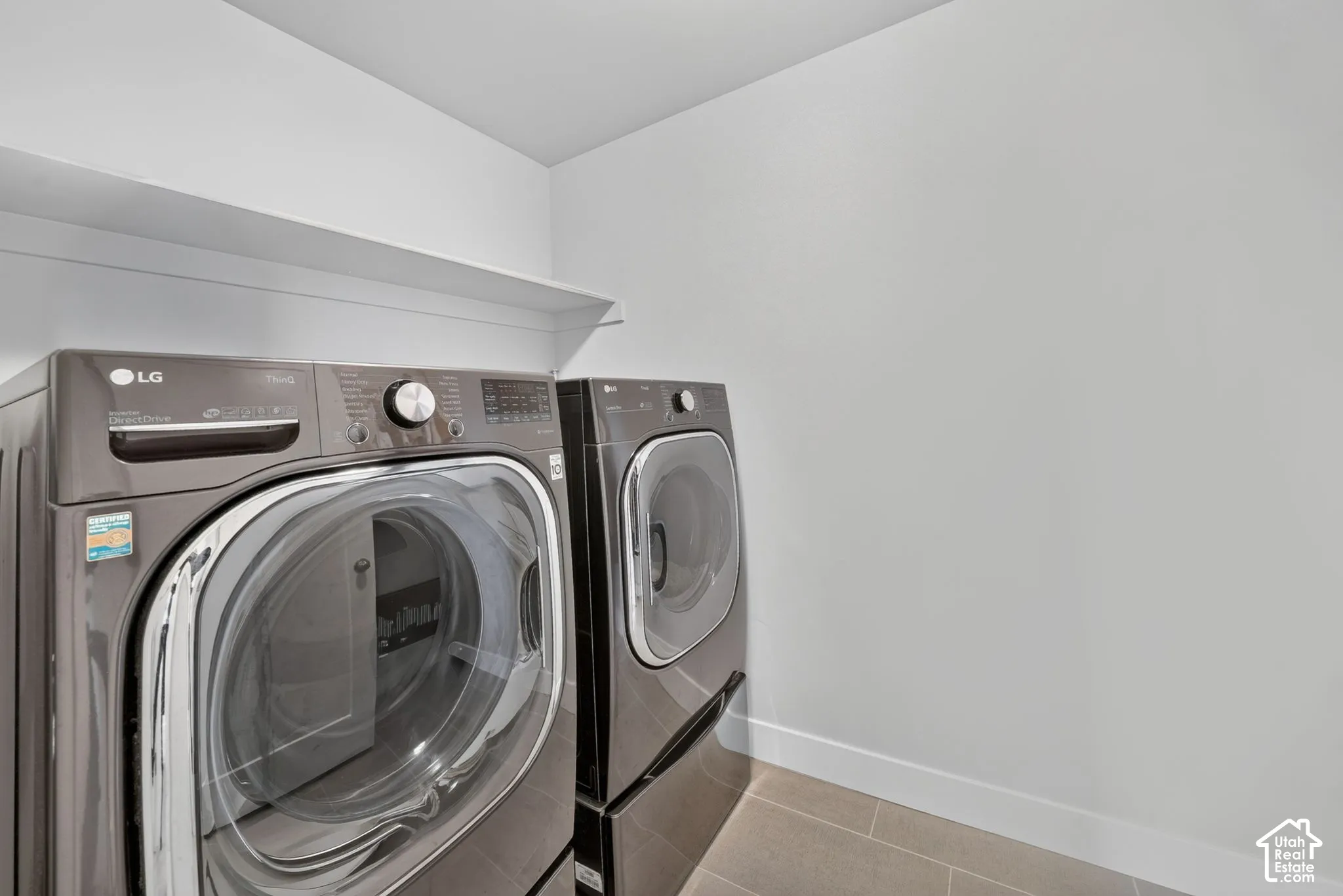 Laundry area featuring large-format tile flooring and overhead built-in shelving