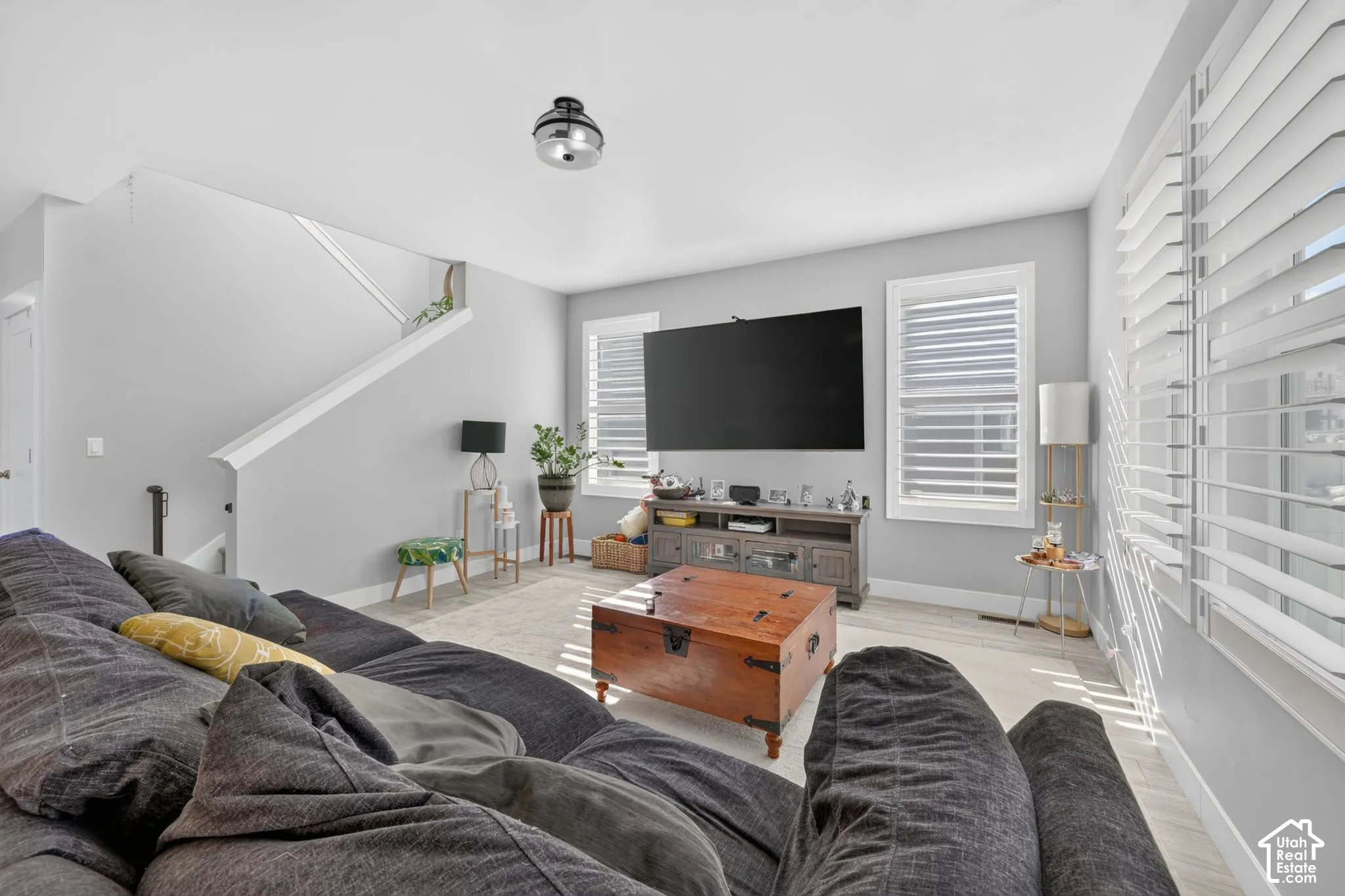 Living area featuring wood-finish flooring, plantation shutters, and a central flush-mount light fixture