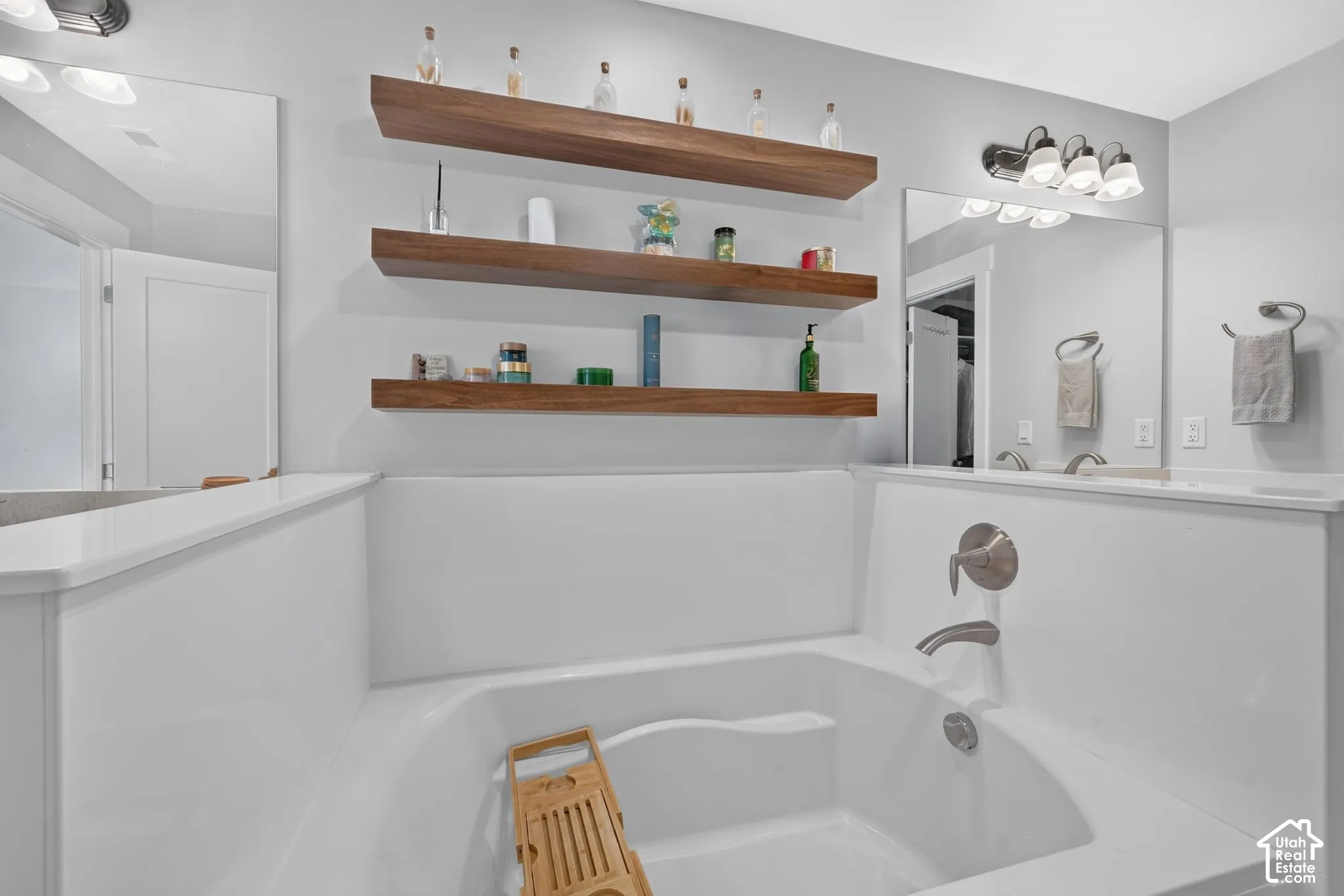 Soaking tub with a white surround and brushed-nickel faucet, complemented by three tiered wooden floating shelves and wall-mounted vanity lighting
