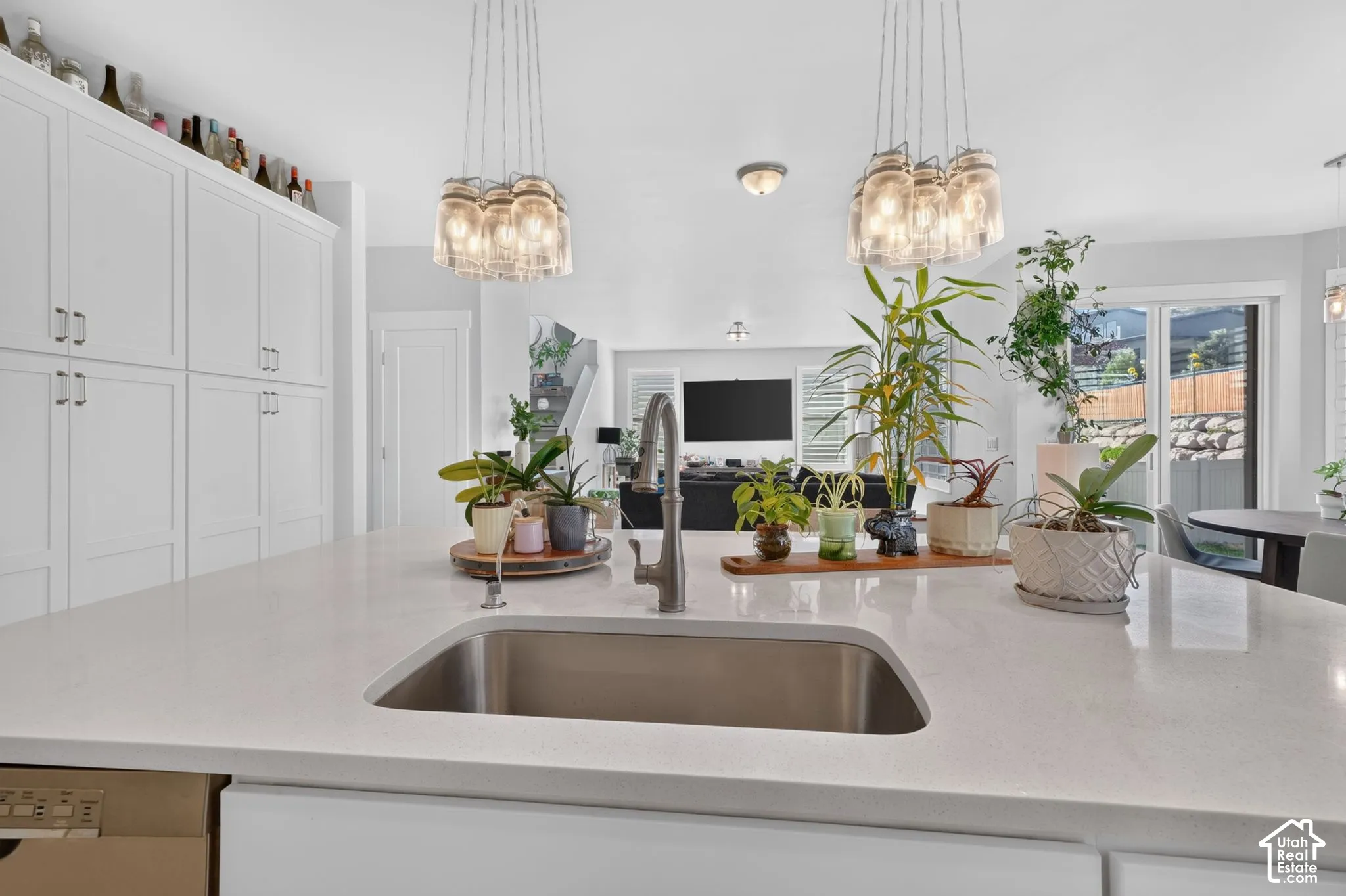 Kitchen island with a quartz countertop, under-mount stainless steel sink, gooseneck faucet, floor-to-ceiling white cabinetry, and multi-light cluster pendant fixtures