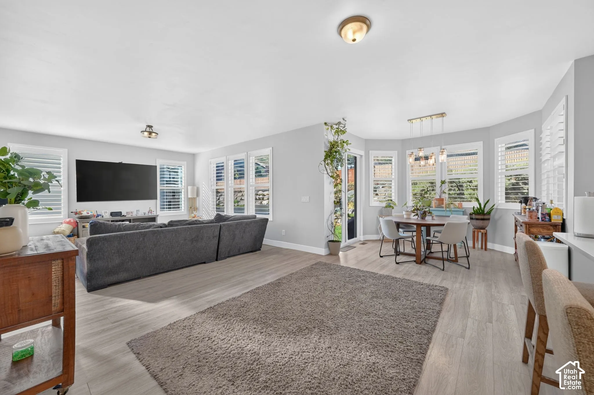 Open-concept interior featuring light wood-finish flooring, recessed lighting, a multi-paneled bay window, sliding glass door, and interior plantation shutters