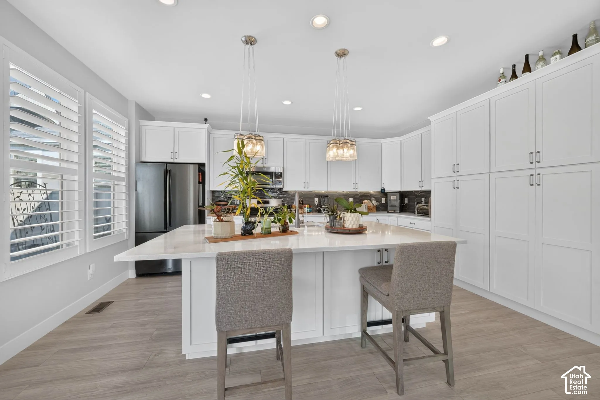 Kitchen featuring a large central island with a stone countertop, white shaker-style cabinetry, stainless steel appliances, recessed ceiling lighting, and wood-finish flooring