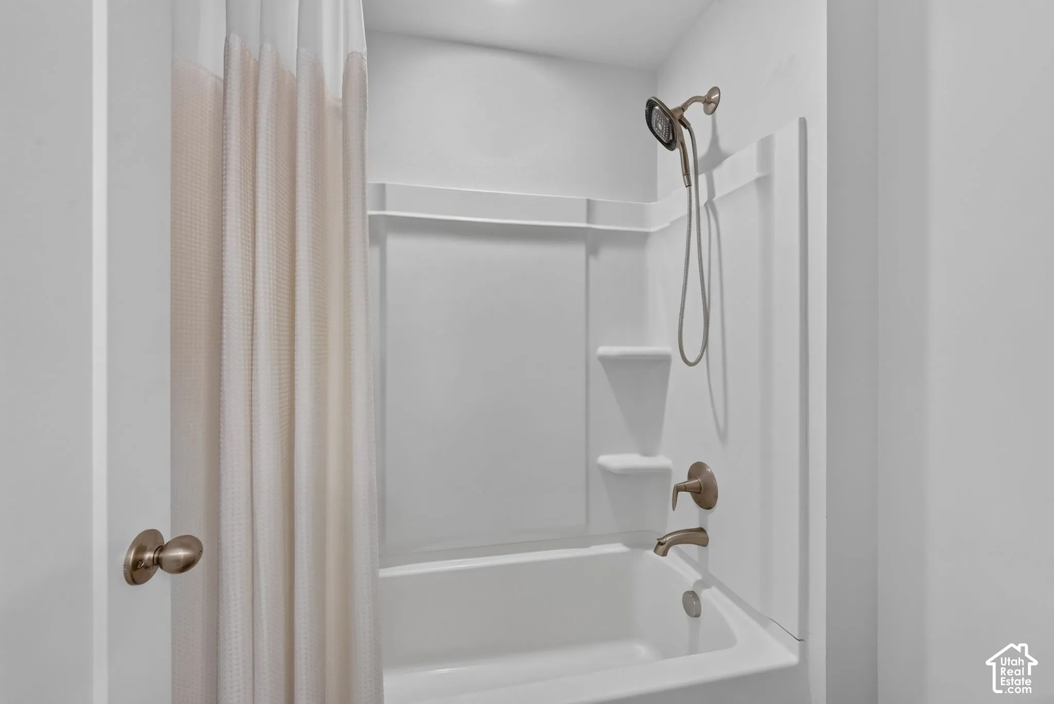 Full-size tub and shower combination featuring a white composite surround with integrated shelving and bronze-tone fixtures