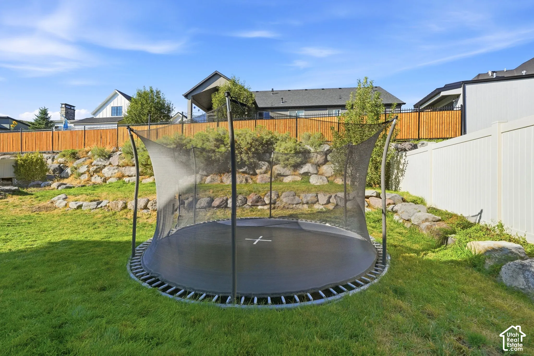 Backyard featuring tiered stone retaining walls, wood-tone privacy fencing, and vinyl perimeter fencing