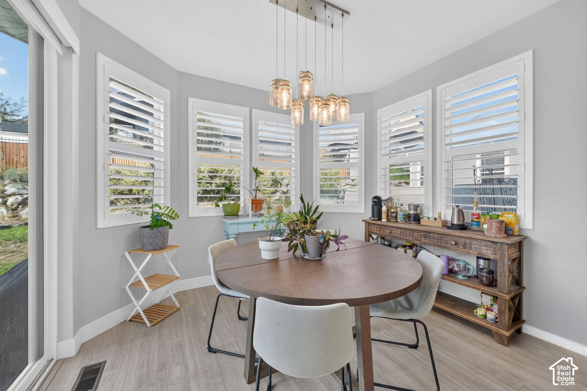 Bay area featuring large windows with plantation shutters, multi-light glass pendant chandelier, wood-finish flooring, and sliding glass door