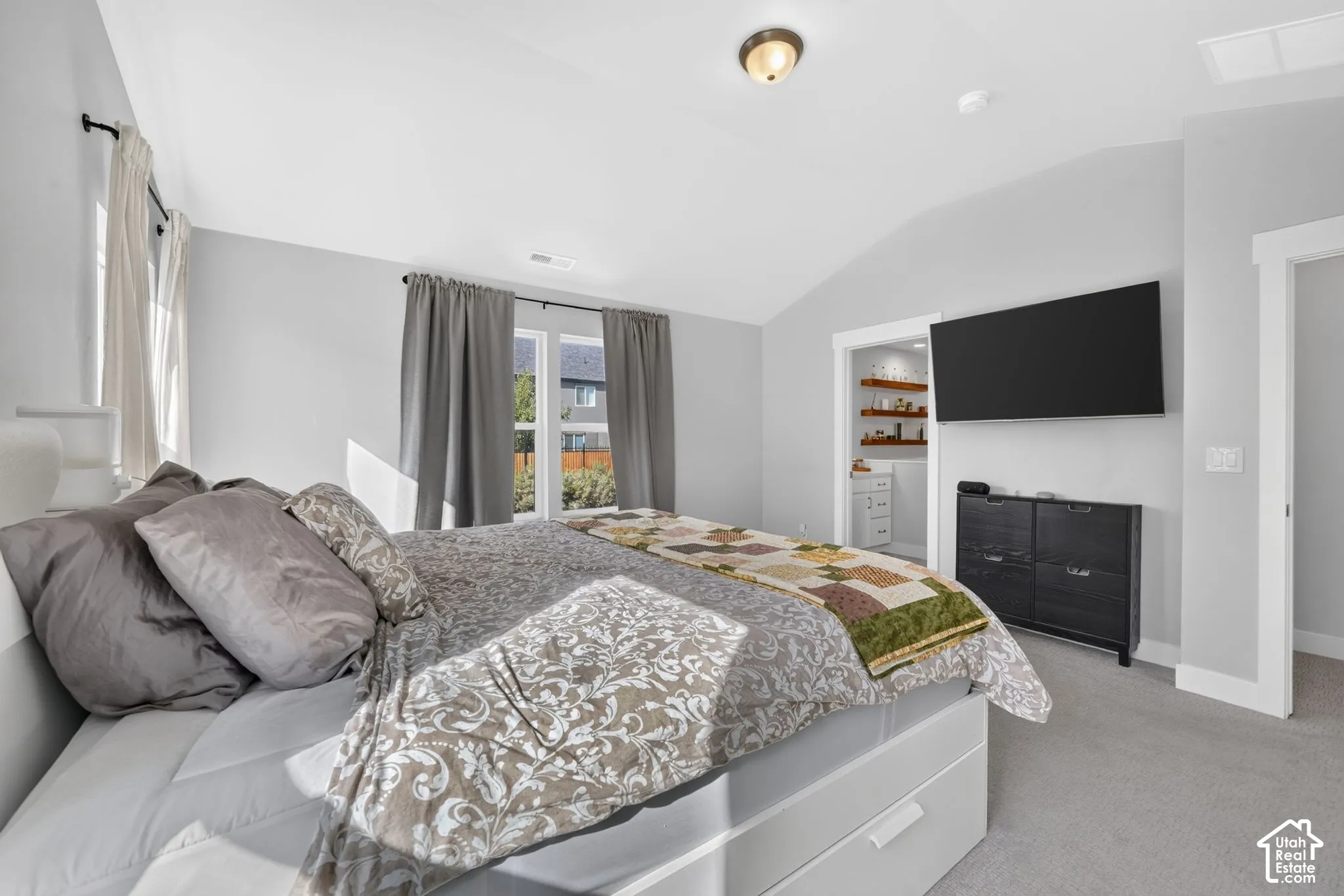 Vaulted ceilings, carpeted flooring, and neutral wall paint featuring white-trimmed door frames and windows