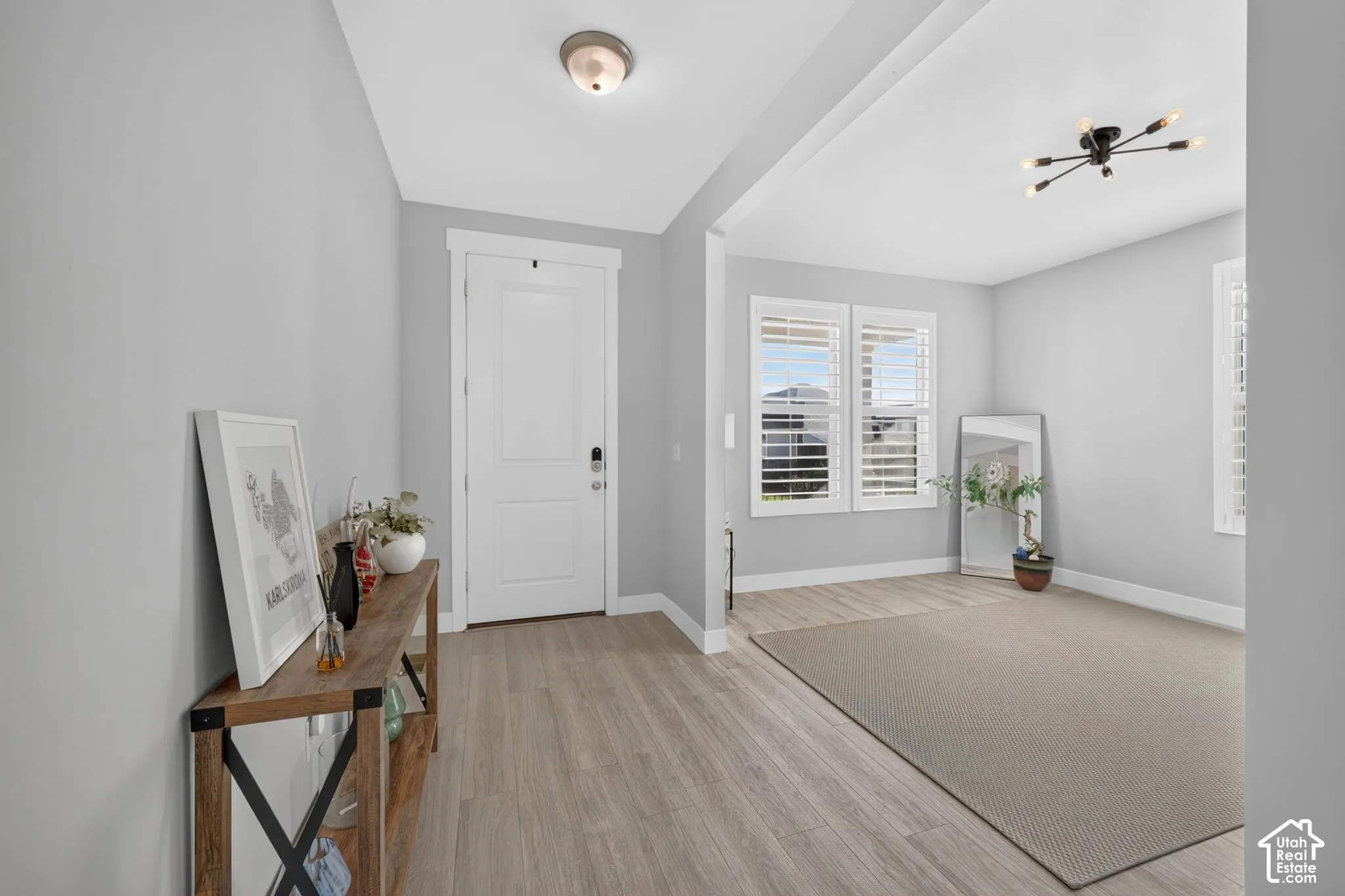 Entry featuring wood-finish flooring, white panel door with electronic deadbolt, multi-arm sputnik-style ceiling light, and windows with integrated shutters