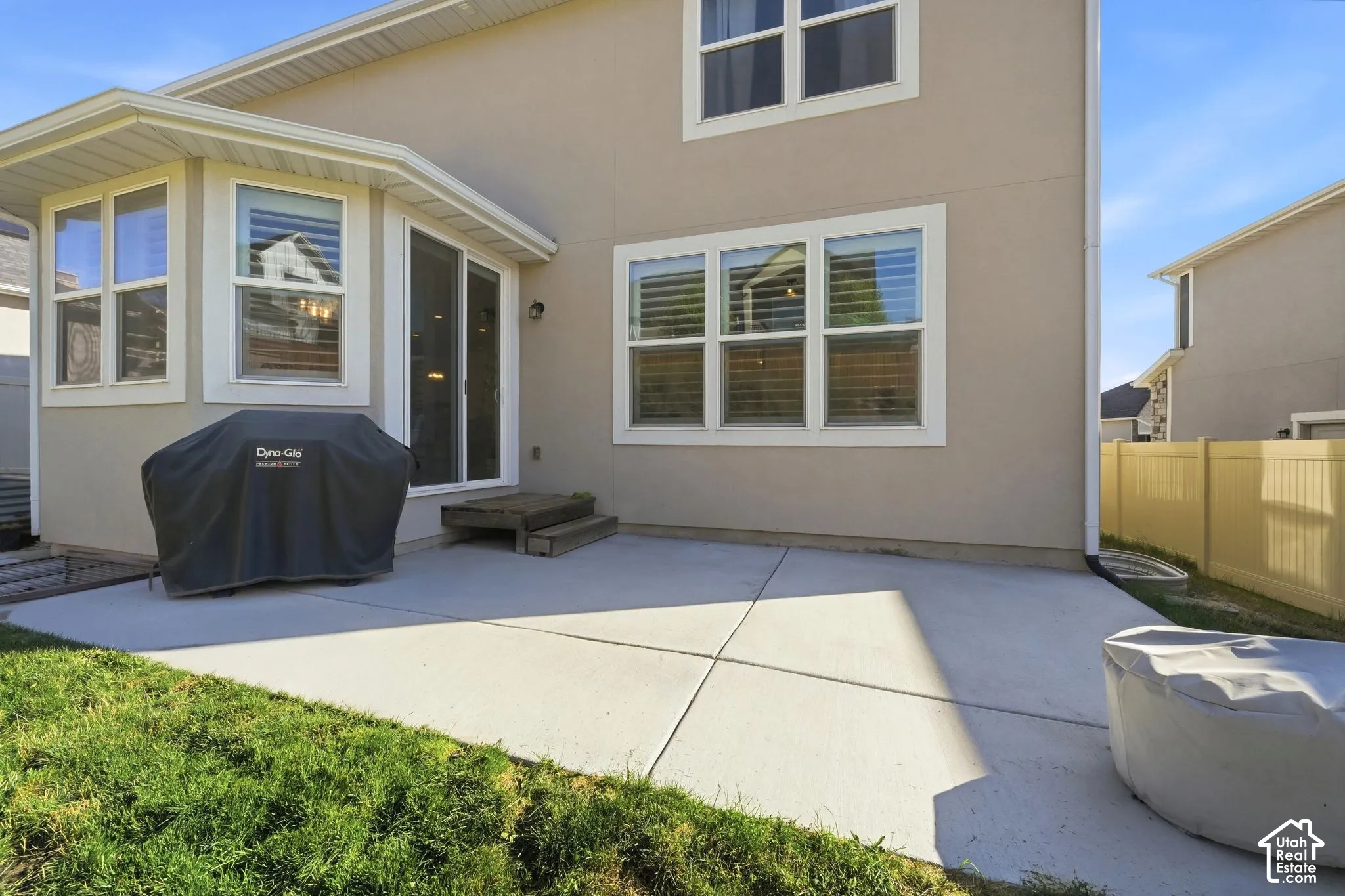 Rear exterior featuring a concrete patio, sliding glass doors, multi-pane windows, and a light-toned stucco facade