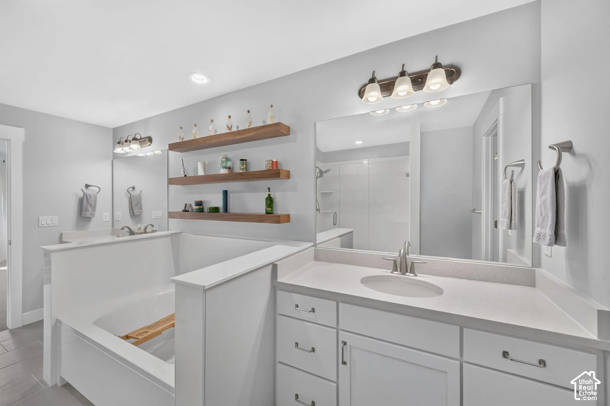 Bathroom featuring a white vanity with composite countertop, drop-in sink, wall-to-wall mirror, built-in soaking tub, and custom wood shelving