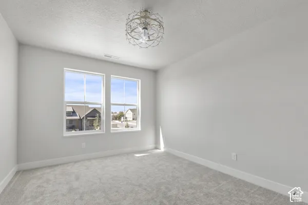 Neutral-toned interior space featuring light-colored wall-to-wall carpeting, dual-pane windows with white casing, and a decorative orb-style chandelier