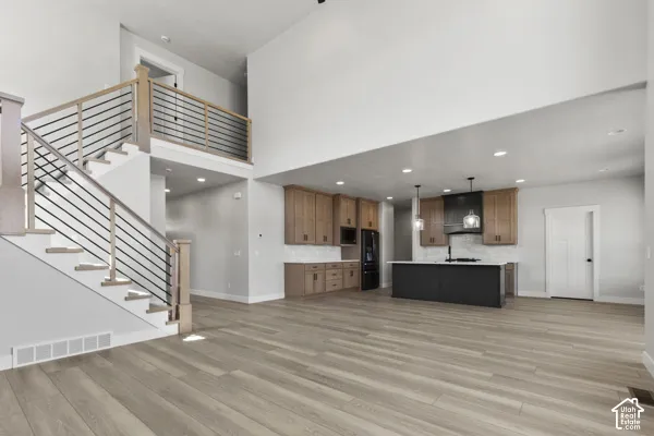 Open-concept interior featuring high ceilings, wood-finish flooring, a kitchen island with a dark base, and a staircase with light-wood handrails and horizontal metal balusters