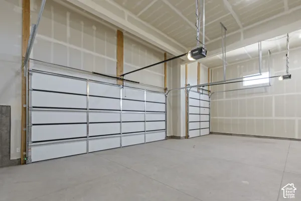 Multi-vehicle garage featuring high ceilings, unfinished drywall, exposed structural wood supports, concrete flooring, and motorized door openers