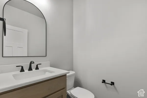 Vanity with wood-finish cabinetry, solid surface countertop, matte black widespread faucet, arched wall-mounted mirror, and matching matte black hardware