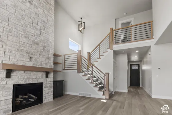 Floor-to-ceiling stone fireplace featuring a wood mantel, wood-finish flooring, floating wood shelving, and a staircase with wood handrails and horizontal metal balusters