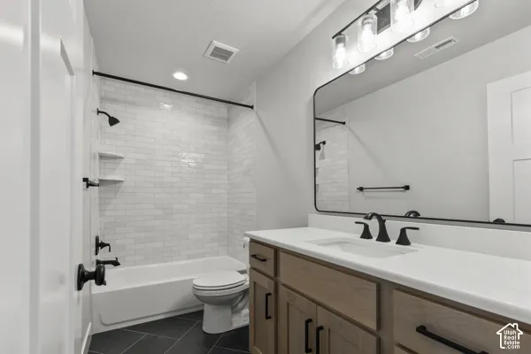 Bathroom featuring a vanity with light-tone wood cabinetry, a solid surface countertop, white subway tile shower surround, matte black hardware, and an oversized rectangular mirror