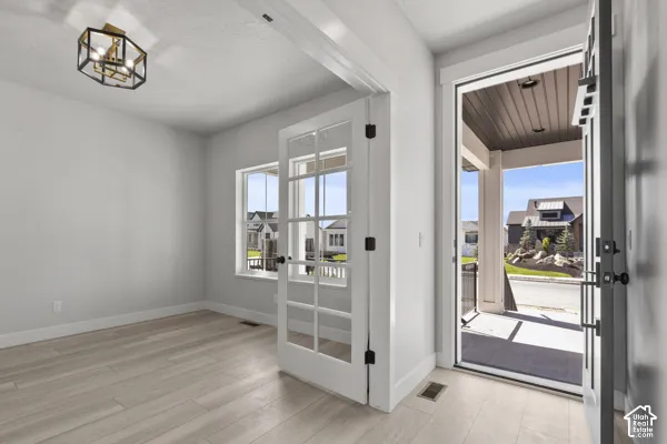 Interior space featuring wood-finish flooring, a geometric metal chandelier, white-framed windows, and white French doors opening to a covered exterior porch