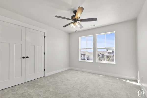 Room featuring neutral wall-to-wall carpeting, dual-pane windows, a ceiling fan with integrated lighting, and a double-door closet with dark hardware