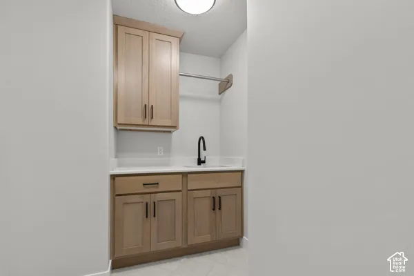 Custom wood-finish cabinetry, solid-surface countertop, undermount sink with matte black faucet, and mounted metal garment rod
