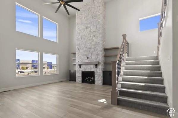Double-height ceiling, floor-to-ceiling stone fireplace, built-in shelving and cabinetry, large windows, and staircase with metal railings