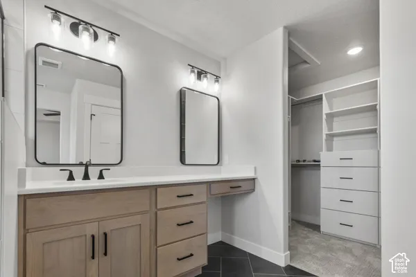 Dual-sink vanity featuring light wood-finish cabinetry, white countertop with integrated sinks, matte black hardware, rectangular mirrors with black frames, and custom built-in closet shelving