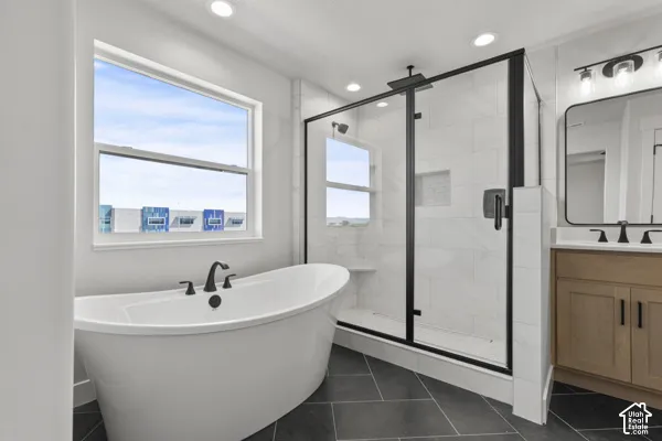 Freestanding soaking tub with matte black faucet, glass-enclosed shower with tiled surround and black hardware, wood-finish cabinetry, and recessed lighting
